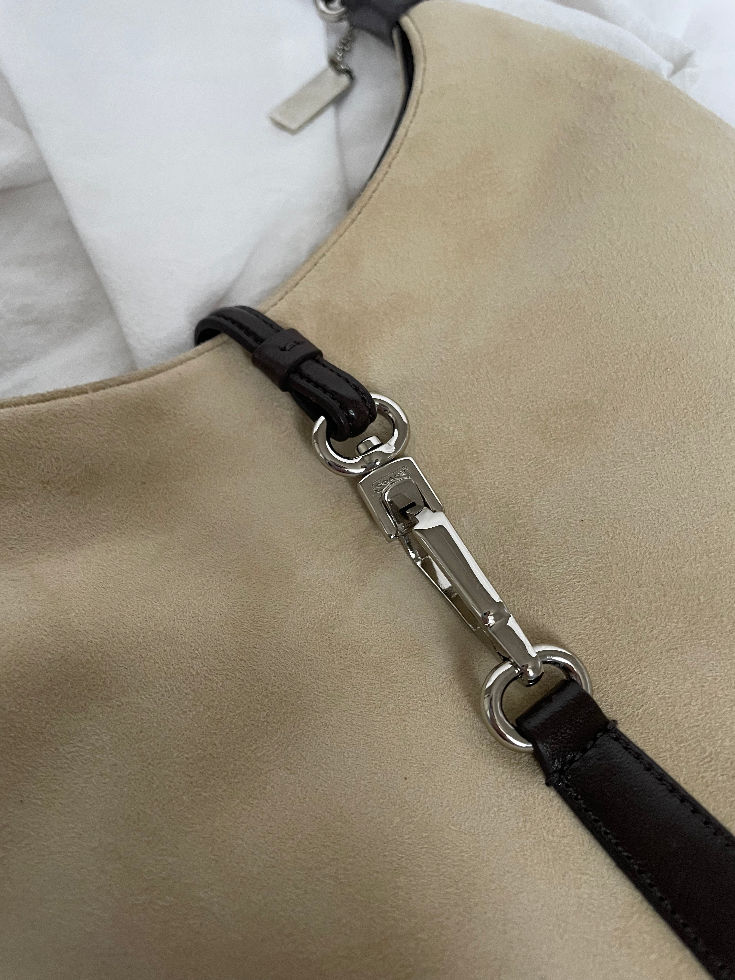 A vintage Coach shoulder bag from 2001 in beige suede with dark leather accents. The bag features a sturdy leather strap, silver-tone hardware, and a functional clasp detail on the front.&nbsp;