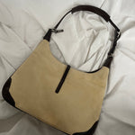 A vintage Coach shoulder bag from 2001 in beige suede with dark leather accents. The bag features a sturdy leather strap, silver-tone hardware, and a functional clasp detail on the front.&nbsp;