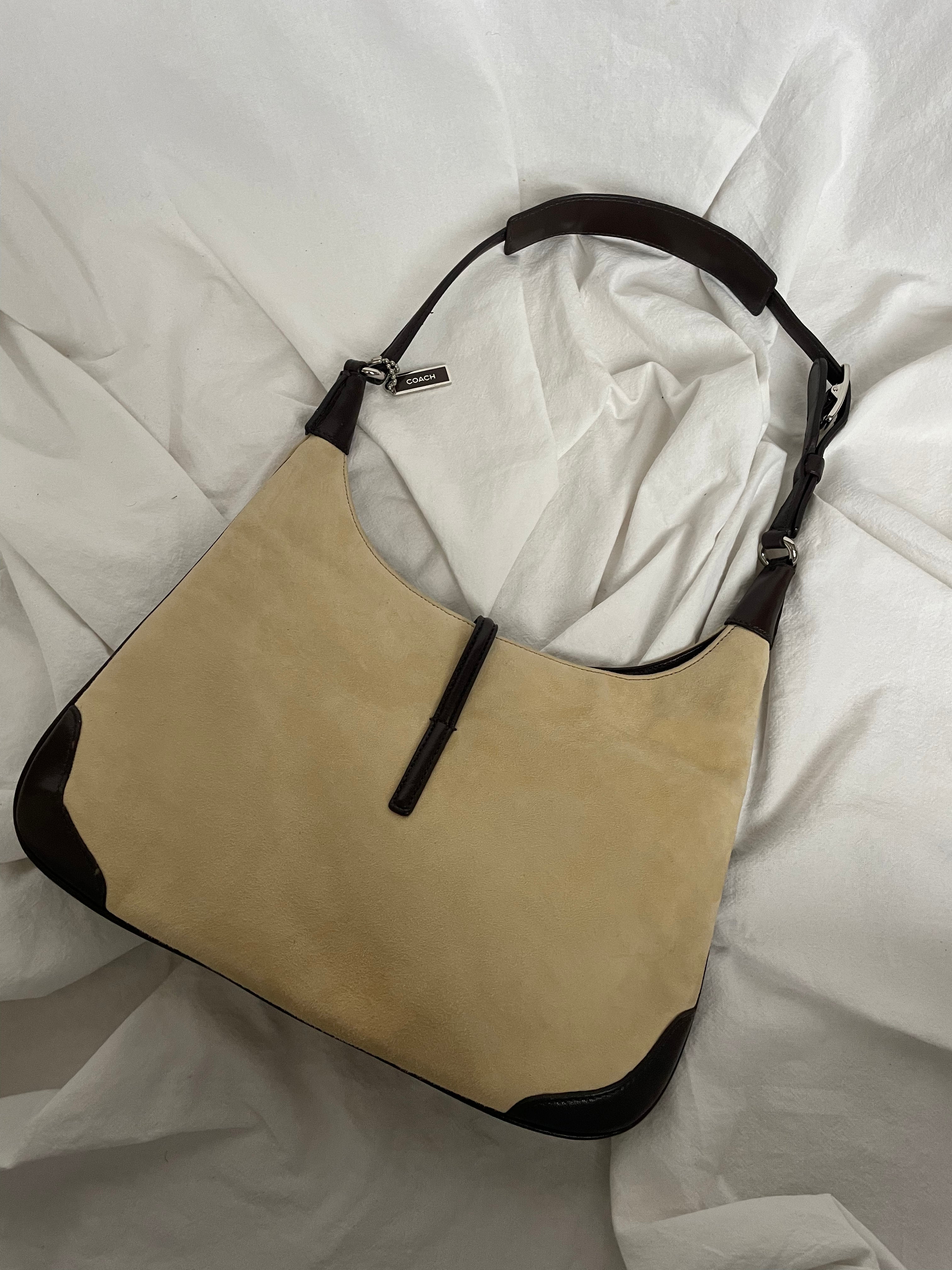 A vintage Coach shoulder bag from 2001 in beige suede with dark leather accents. The bag features a sturdy leather strap, silver-tone hardware, and a functional clasp detail on the front.&nbsp;