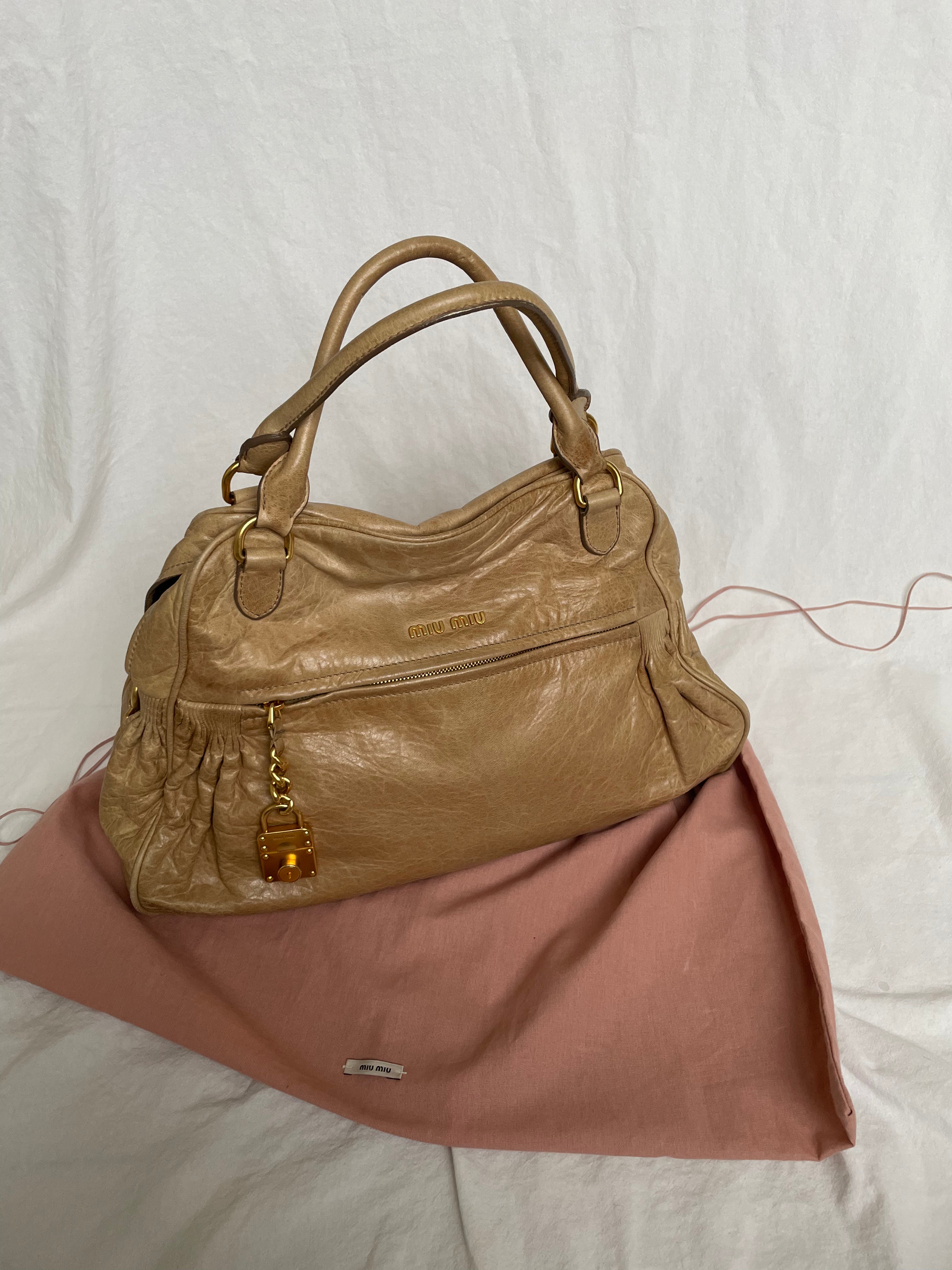 Miu Miu leather handbag.&nbsp;Crafted from matelassé calf leather, this handbag features luxurious lambskin and gold-tone hardware. It includes a front zip pocket, a top zip closure, and an interior slip pocket. The bag has a gold padlock charm.&nbsp;