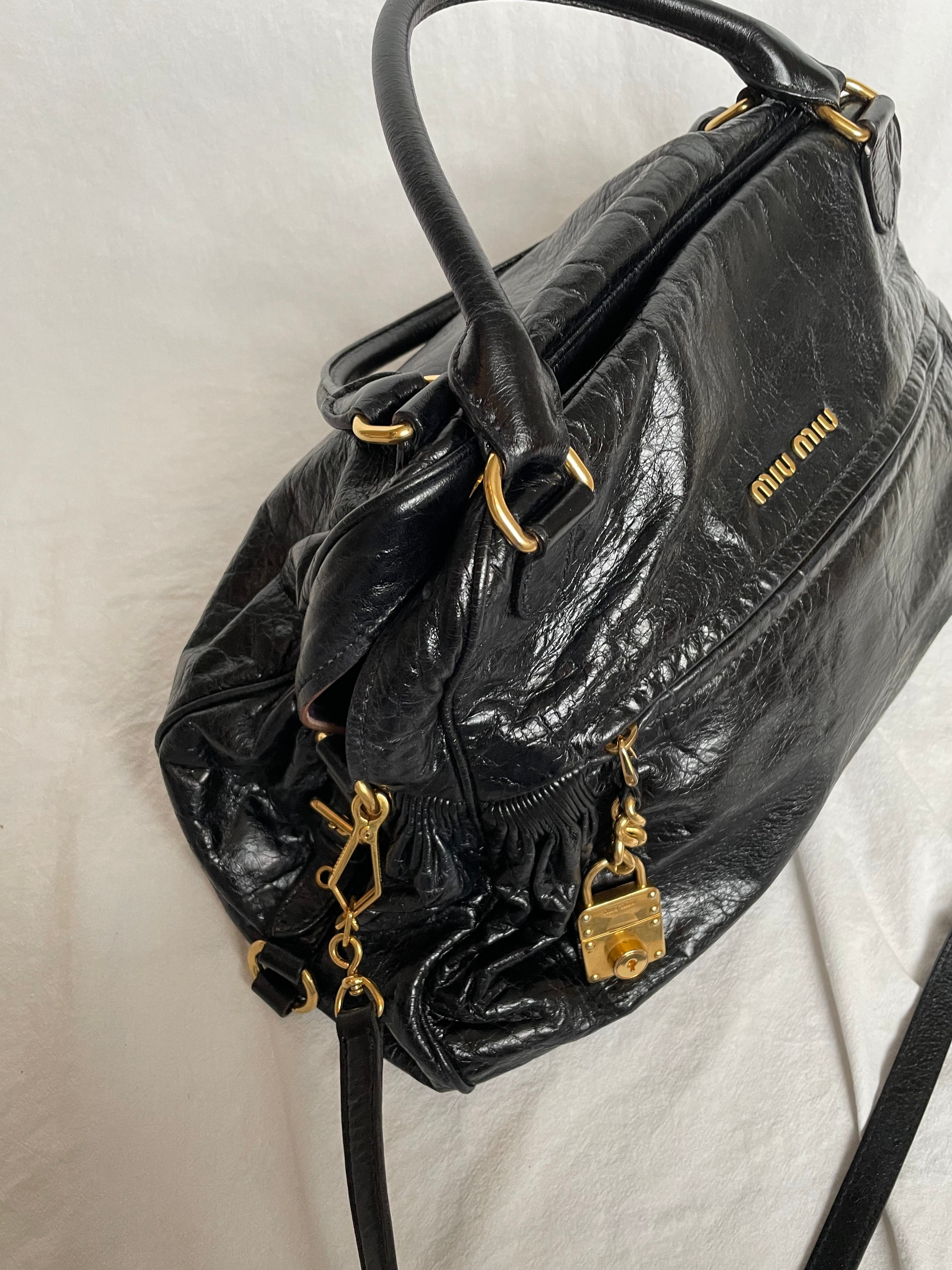 Miu Miu black nappa leather bag in a very good condition.

Crafted from nappa leather, this handbag features luxurious material and gold-tone hardware. It includes a front zip pocket, a top zip closure, and an interior slip pocket. The bag has a gold padlock charm.