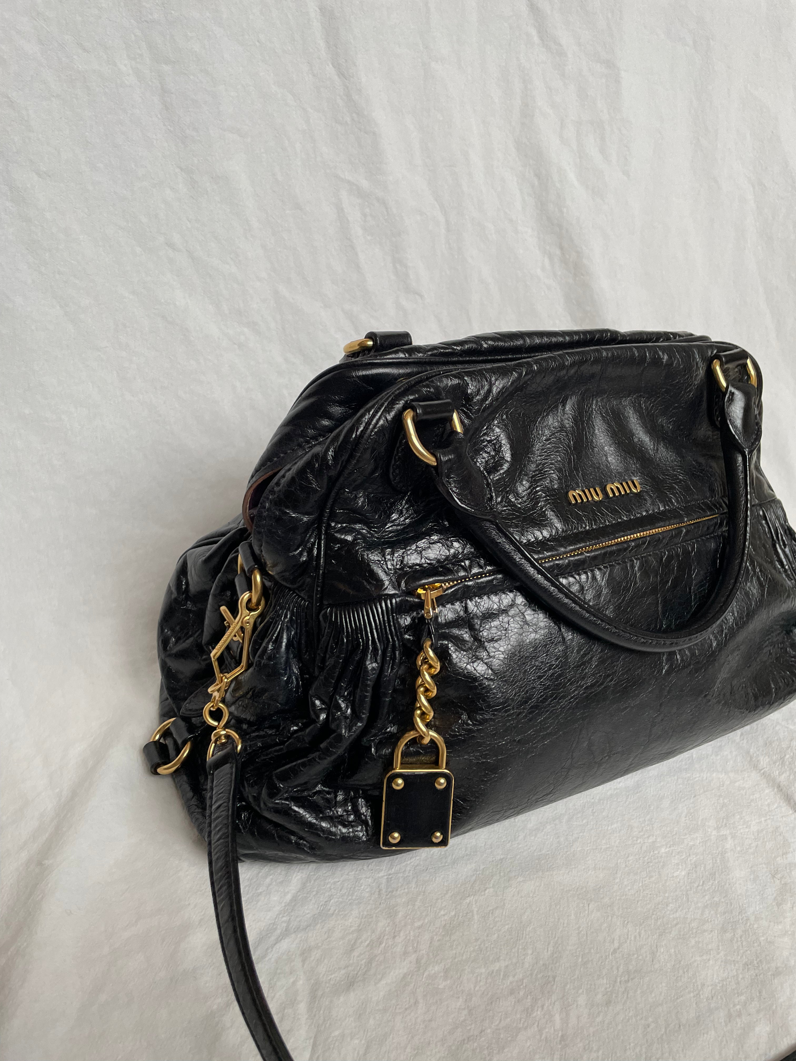 Miu Miu black nappa leather bag in a very good condition.

Crafted from nappa leather, this handbag features luxurious material and gold-tone hardware. It includes a front zip pocket, a top zip closure, and an interior slip pocket. The bag has a gold padlock charm.