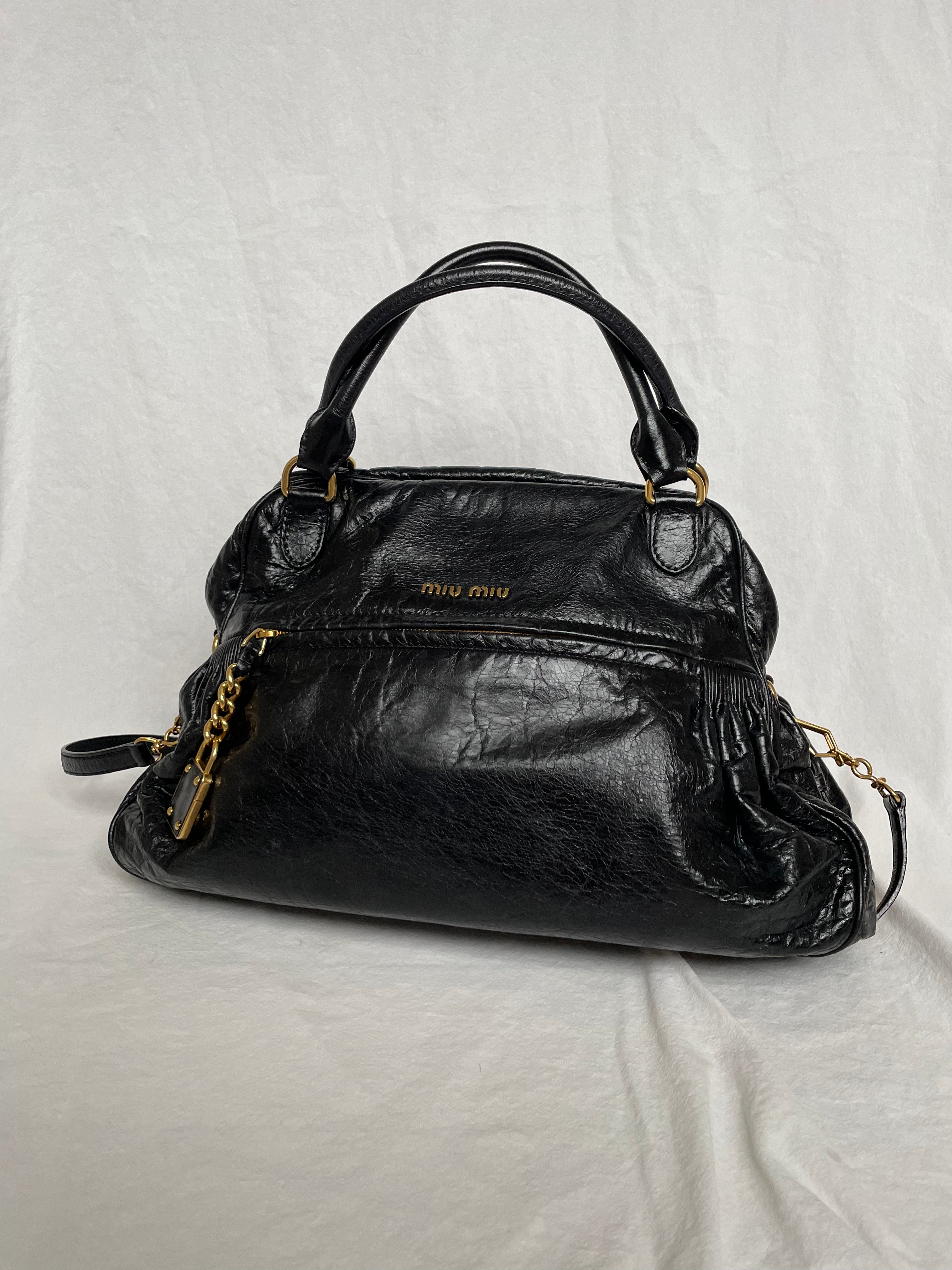 Miu Miu black nappa leather bag in a very good condition.

Crafted from nappa leather, this handbag features luxurious material and gold-tone hardware. It includes a front zip pocket, a top zip closure, and an interior slip pocket. The bag has a gold padlock charm.