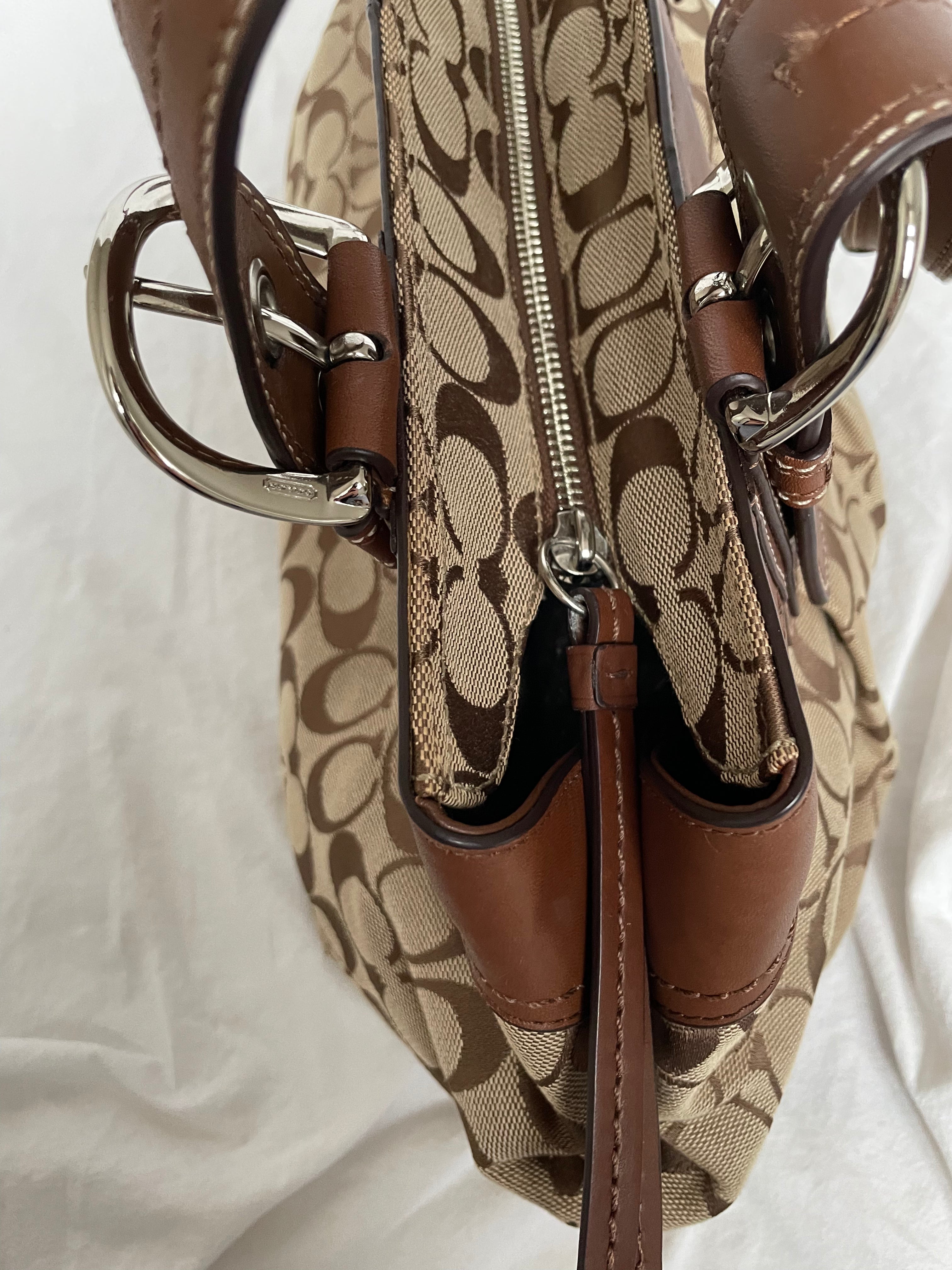 Beautiful Coach bag made from the brand’s signature canvas, with brown leather and silver hardware. Inside, there are three pockets—one with a zipper and two open.