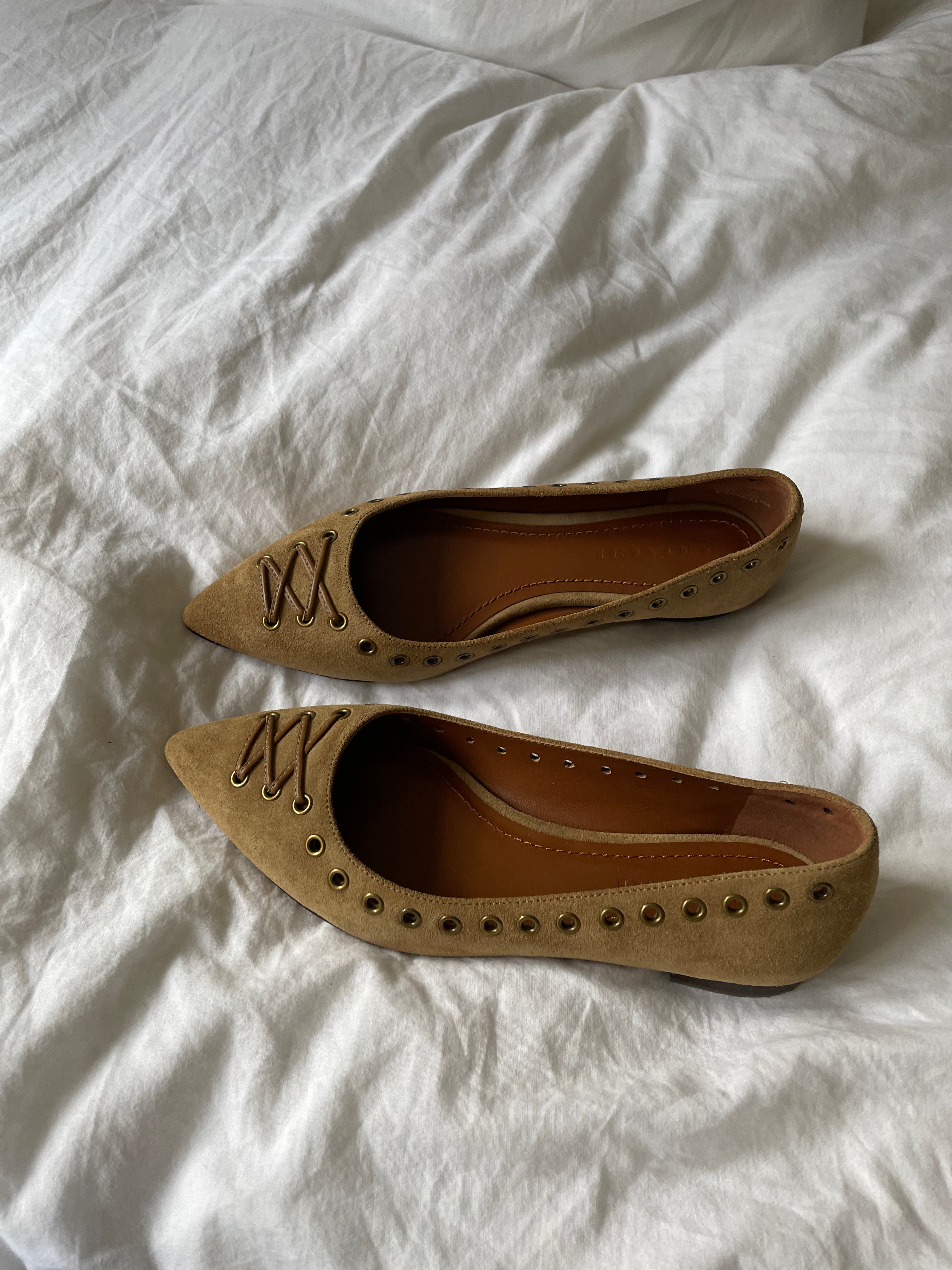 These vintage Coach ballet flats feature a pointed toe, lace-up details, and gold-tone eyelets along the edges. Crafted from beige suede with a smooth leather lining.